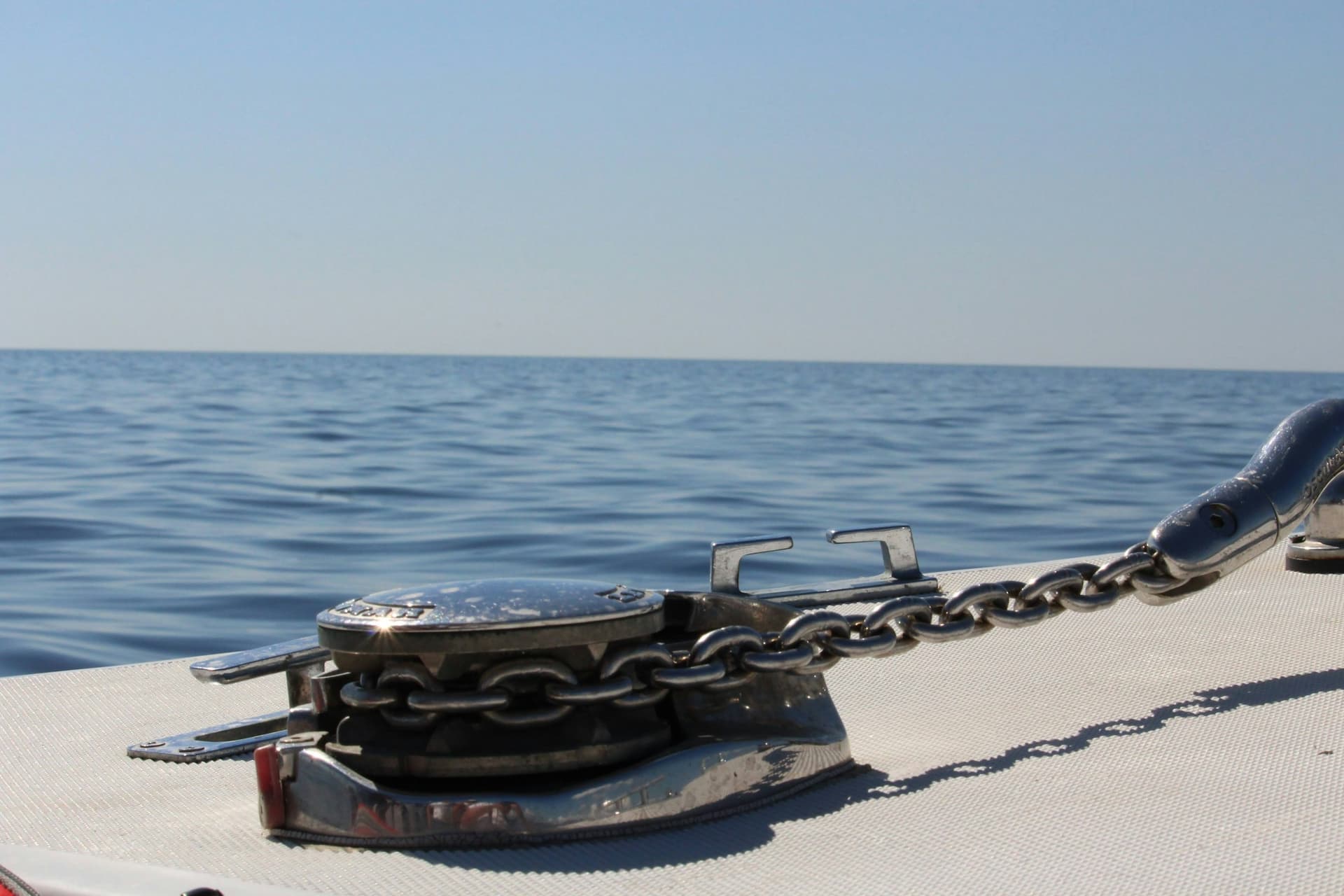 Anchor chain running over a polished windlass on a boat's foredeck toward the bow, with calm open water behind.
