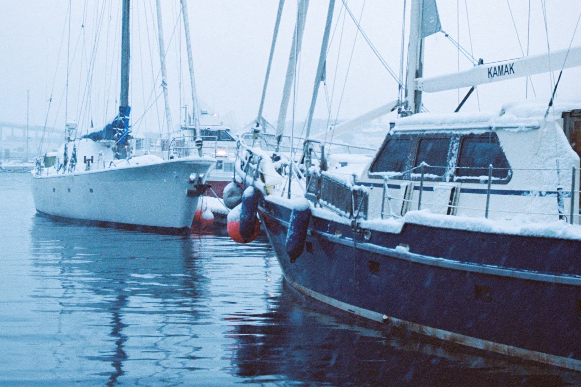 Two cruising yachts moored in a snowy harbour, their decks and deckhouses covered in snow.