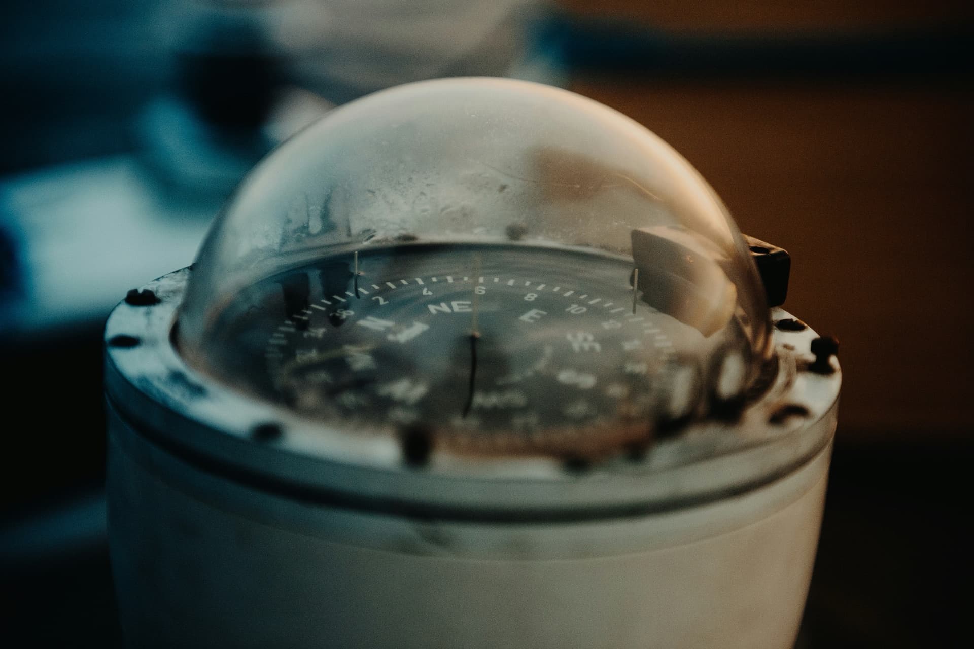 A domed steering compass in a weathered white housing, its card showing NE and E, in warm, low light.
