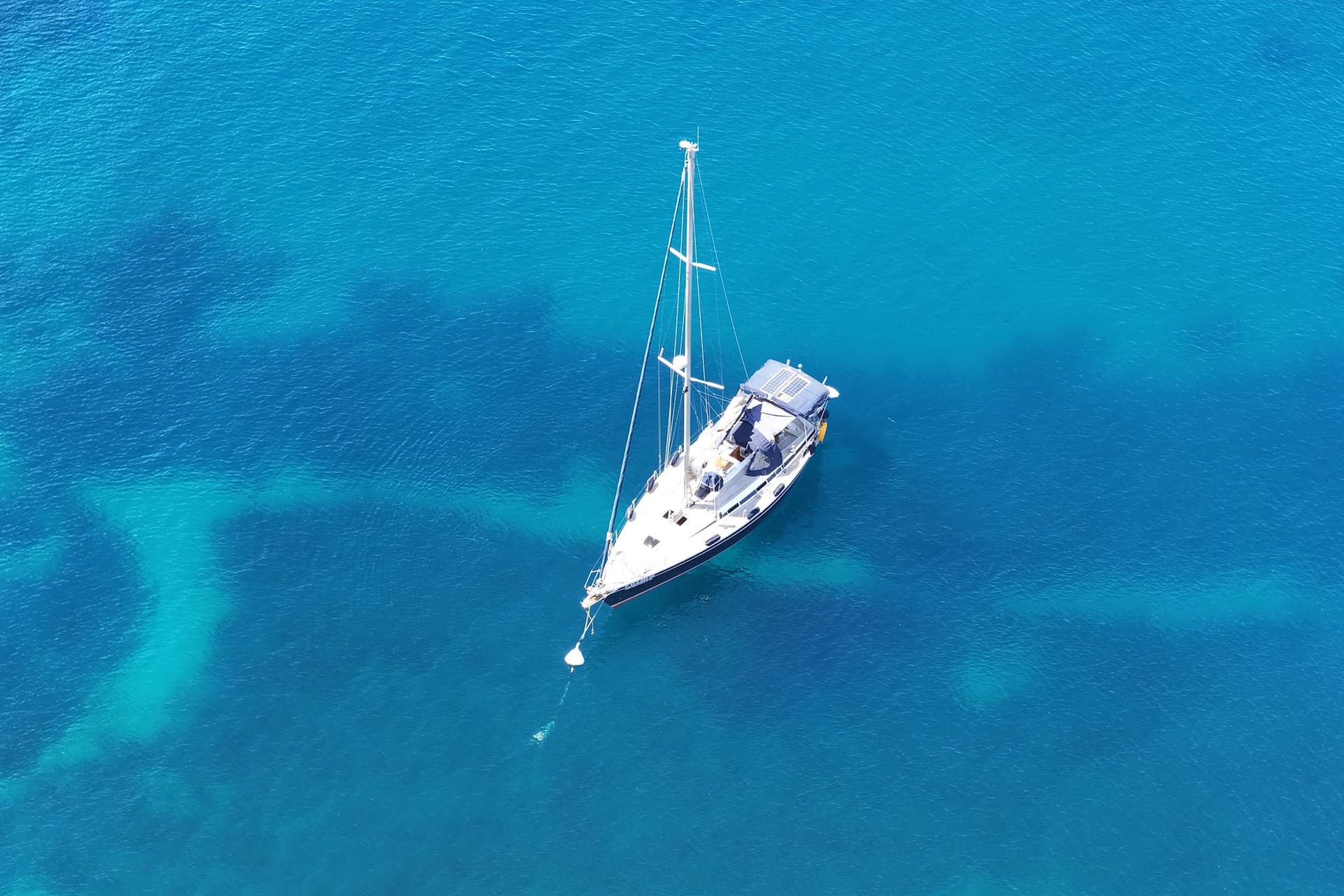 A sailboat on a mooring buoy in clear blue water, seen from above.