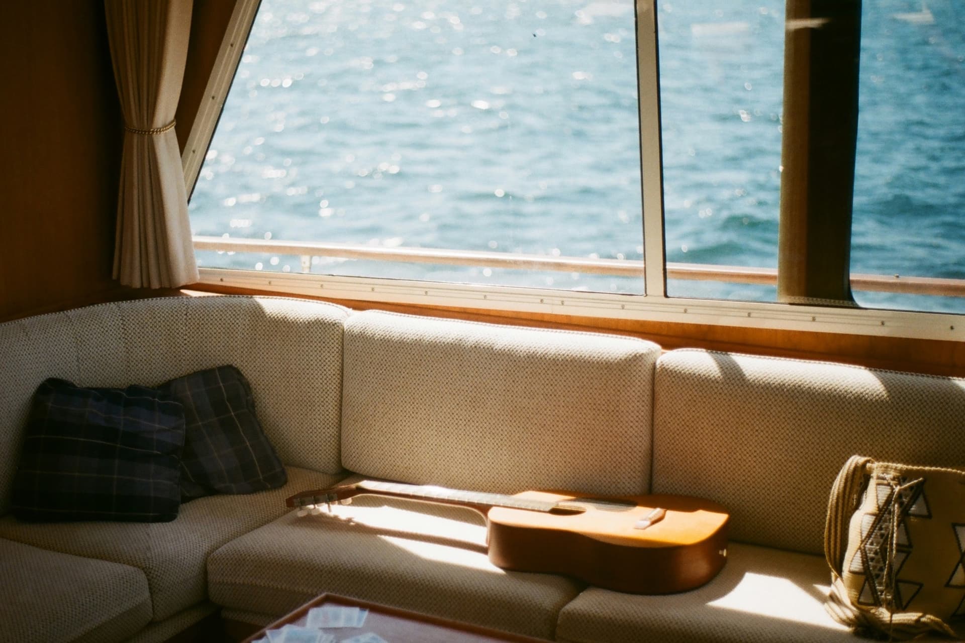 A sunlit boat cabin with a cushioned settee under large windows looking out over open water.