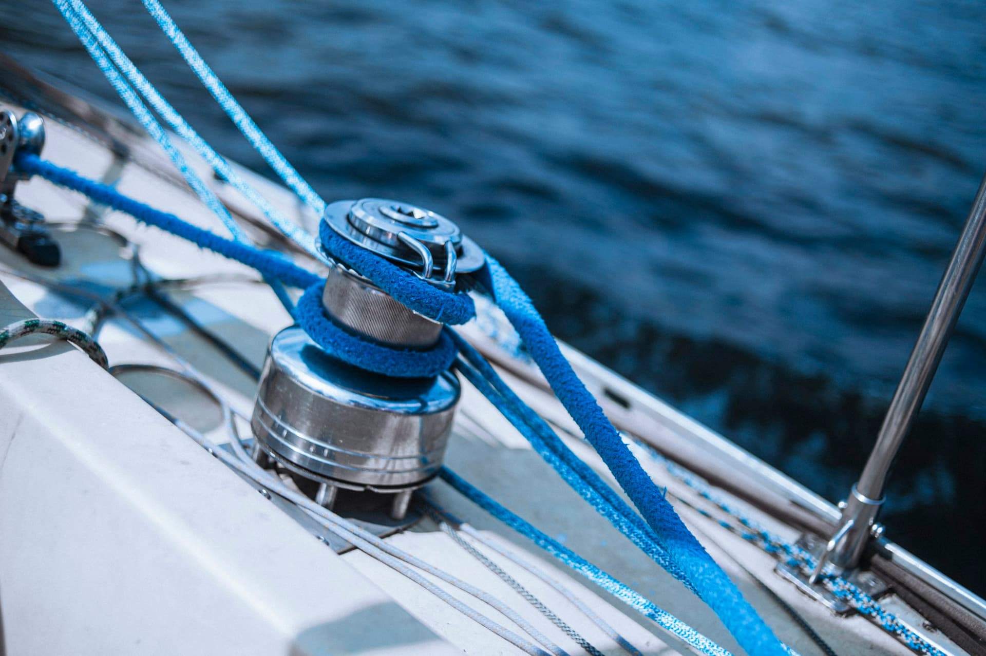A chrome self-tailing winch on a sailboat deck, with blue line wrapped on the drum and led up into the jaws.